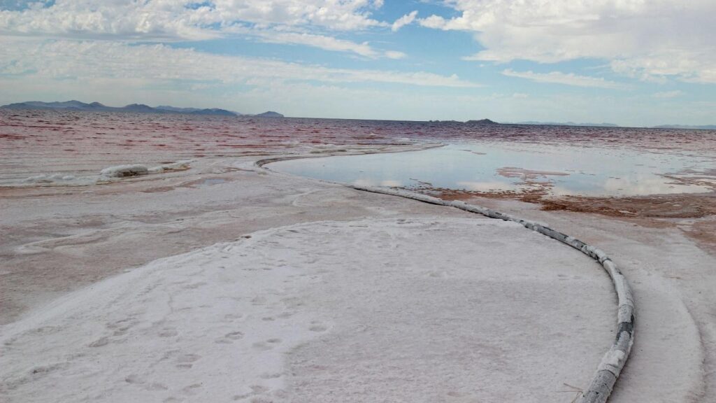 a black hose crusted and partly buried with white and pink minerals winds into a pool of water