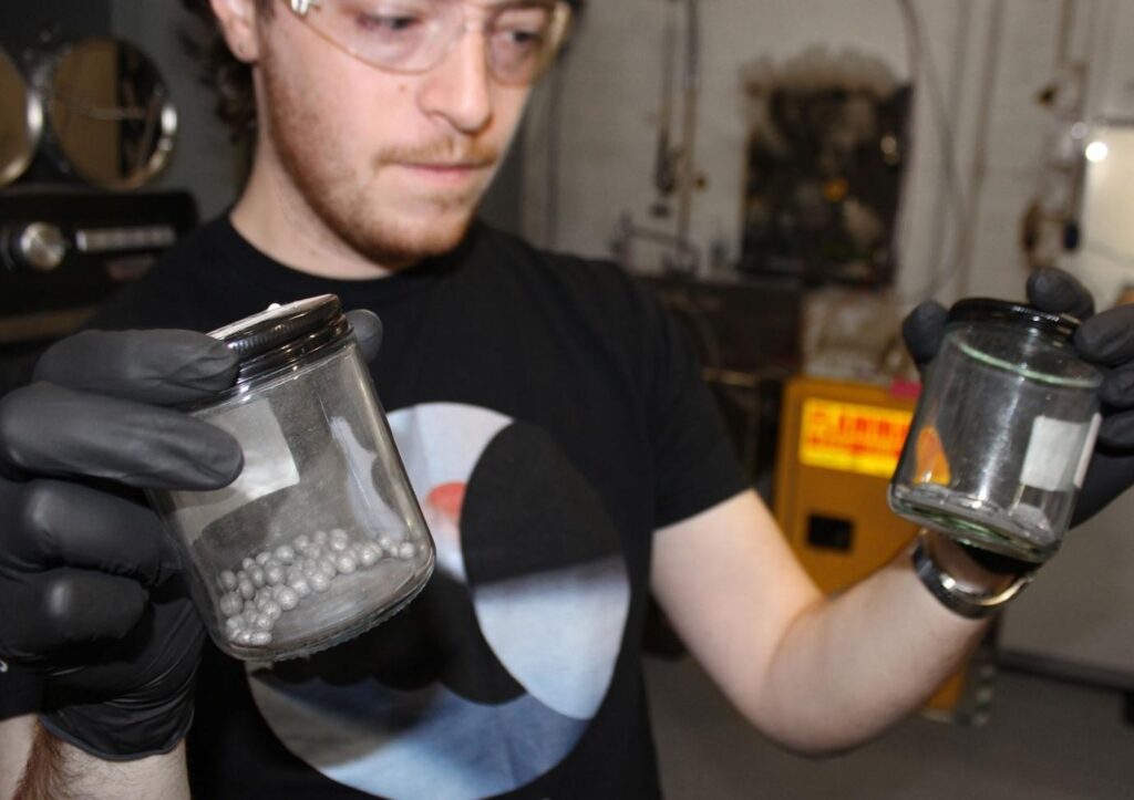 Petert Godart holding up two glass jars; one with metal spheres and the other with flat metal shapes