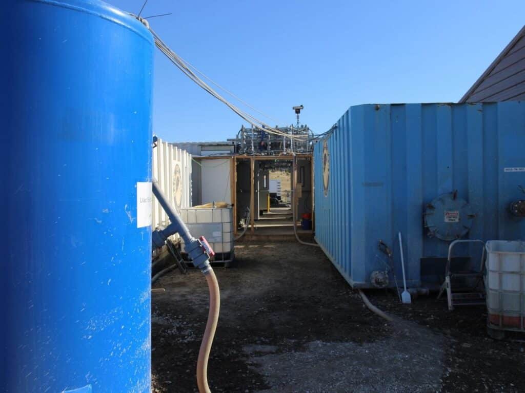 walking path between several tall blue tanks connected by hose