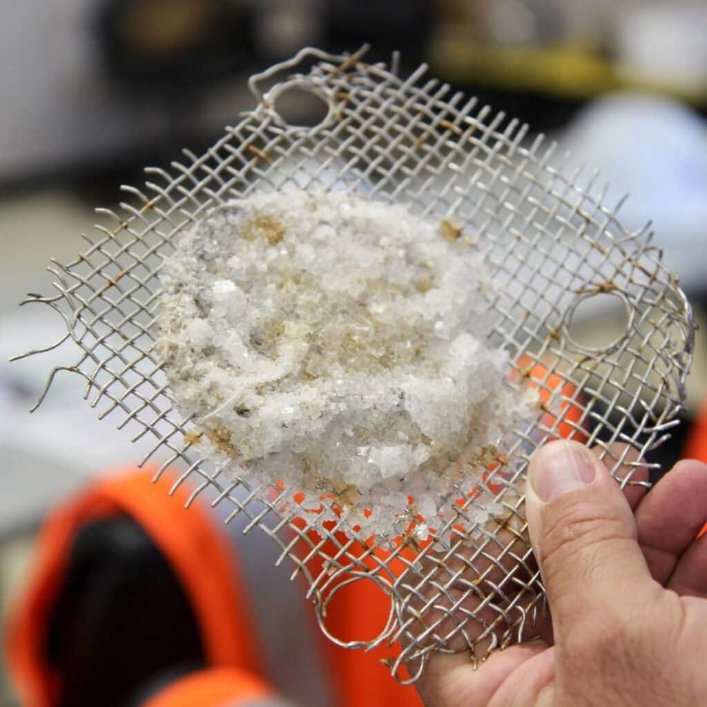 hand holding a square of wire mesh with a clump of crystals in the center