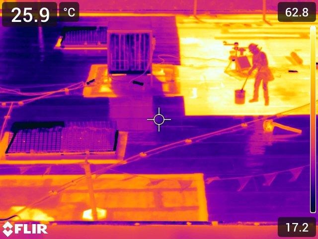 thermal image of a person on a rooftop holding a stick in a bucket